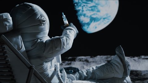 Back view of lunar astronaut having a beer while resting in a beach chair on Moon surface, saluting to Earth. Shot with 2x anamorphic lens