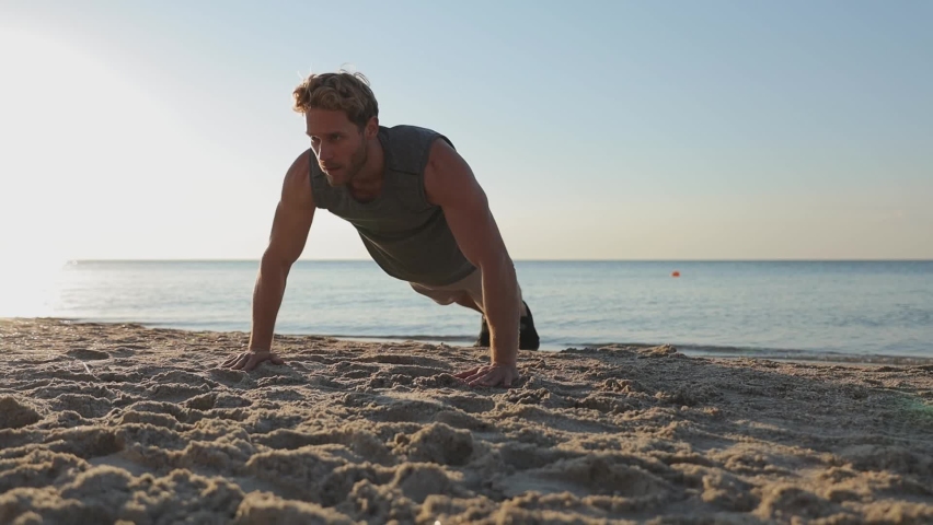Strong sporty athletic toned fit sportsman man 20s wear sports clothes warm up training doing push-ups exercises on sand coast at sunrise sun dawn over sea beach outdoor seaside in summer day morning Royalty-Free Stock Footage #1074667295