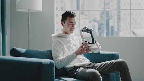 Joyful Asian consumer in hoodie puts on virtual reality headset and fixes with hands before playing simulation game slow motion