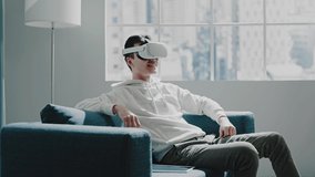 Asian VR tester guy in white hoodie looks around wearing headset and smiling in room with large window and floor lamp slow motion