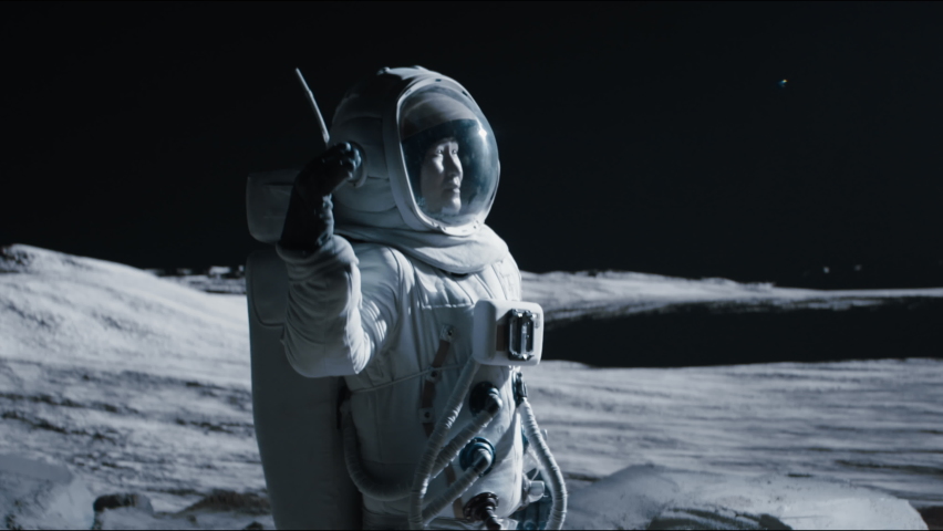 MID JIB Portrait of Asian lunar astronaut opens his visor while exploring Moon surface. Shot with 2x anamorphic lens Royalty-Free Stock Footage #1074671843
