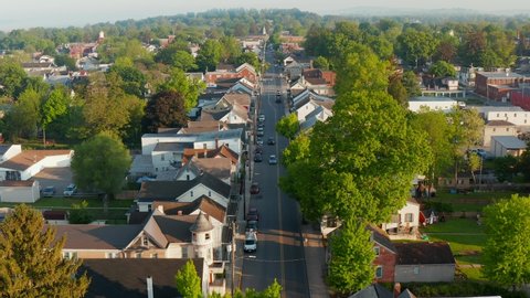 Rising aerial reveals Small Town America. School bus drives on street through community. Houses and homes in quiet quaint residential suburb in USA. Beautiful establishing shot in golden hour.
