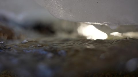 Close up of snow and ice dripping water drop into mountain stream slow motion
