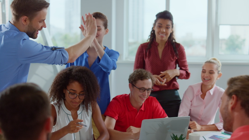 Group of creative colleagues working with blueprint indoors. Successful entrepreneurs giving high five in modern office. Happy business people finishing work in meeting room interior. 