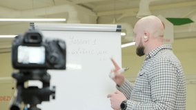 Teacher records video lessons to the camera, he stands and writes with a pen on a flip chart.