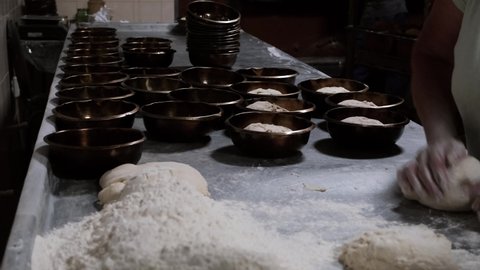 Female baker forming pieces of dough to baking bread on a big table and puts the dough in the prepared molds for the oven. Bakery baking process in factory. Process of preparing bread dough.