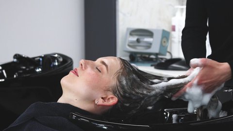 Master woman hairdresser washes hair of a girl with shampoo before styling in a beauty salon.
