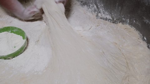 Female baker working in bakery making fresh dough for sourdough bread. Worker pick up lumps of dough ready for production of bread in a factory. Female hands takes dough from an industrial mixer 4k