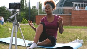 hispanic woman blogger in sportswear shoots video on camera phone as she does yoga on mat in summer park outdoors