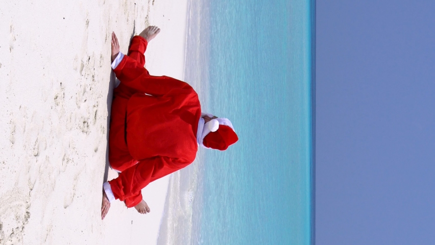 Santa Claus on tropical beach with white sand and azure sea water. Christmas holidays on islands. Vertical format video