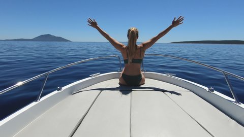 Slow motion - Woman holding out her arms up in the air while sitting on the front of the speedboat. Young adult female enjoying fast ride on a motorboat. Feeling alive, energised and free concept