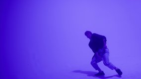 Young blonde guy dancing modern choreography on purple background in studio. Talented choreographer man showing the new hip hop movements. Shooting a dance video clip. Hip hop school for teenagers. 