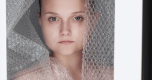 Covid-19 fashion. Pandemic self isolation. Stay safe. Social distancing. Confident female model with bare shoulders posing in protective plastic bubble wrap drop curtain.