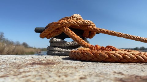 Mooring rope on an iron bollard is twisted into knot and keeps yacht in marina against the blue sky