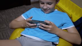Smiling Boy Sit Plays a Mobile Game on Smartphone at Home in Relaxed State. Addicted to online video games. Teen entertainment. Concept of technology and Internet addiction. Close-Up. Slow-motion