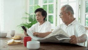 Senior Asian couple having breakfast together in dinner room. 70s retired elderly man reading newspaper while woman using mobile phone - Powered by Shutterstock - Get 15% off with code: PIKWIZARD15