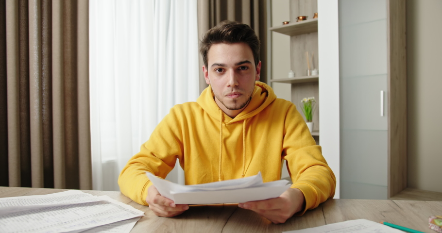 Funny man in yellow hoodie throws papers at wooden table