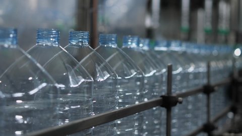 Empty plastic bottles with a volume of 5 liters move along the conveyor in the workshop of the mineral water bottling plant. Production of drinking water at a food processing plant