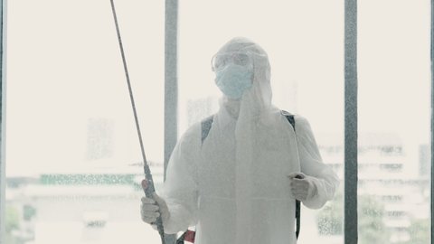 Slow motion of a medical staff in PPE suit and face mask using disinfectant spray in office. Cleaning and sterilizing the work space to prevent spread of Covid-19.