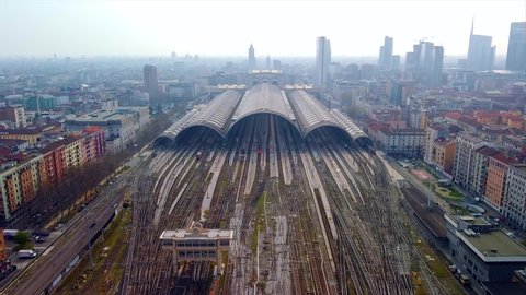 Aerial view of the station. Trains arrive at the station. An old wide arched structure of metal and glass above the station pillars. Tourism. Skyline with tall buildings. Italy, Milan, June 2021 