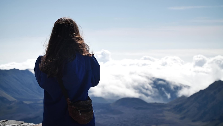 Young woman photographing clouds above the mountains in Haleakalā National Park, Maui, Hawaii. Mid angle, parallax movement, slow motion, HD.