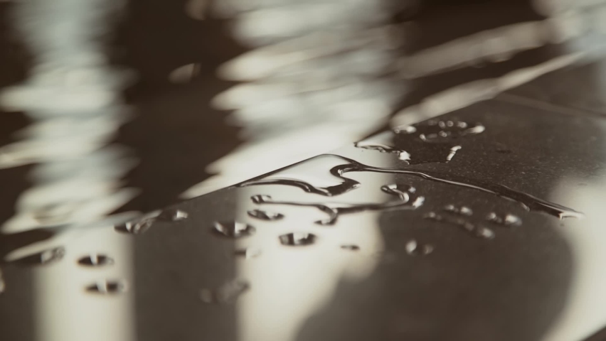Water droplets on black marble tile border of the pool. Water sways in background, close-up.