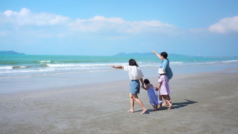 Asian family on summer vacation. Parents with two child girl kid walking on the beach with playing sea water together. Two sisters sibling having fun outdoor lifestyle activity with father and mother.