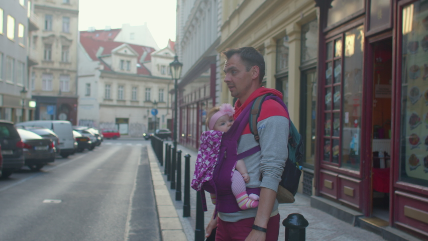 Man dad holding small child in sling. Waiting for taxi car in city. Embracing the lifelong benefits of attachment parenting, practicing babywearing for closeness. Parental involvement for new parents. Royalty-Free Stock Footage #1074726092