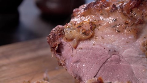 Close-up tracking shot of slicing a baked pork shoulder with a chef knife