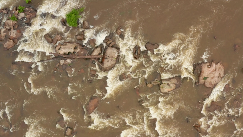 Rising aerial top down reveals rocky James River in Virginia USA. Brown muddy water after rain and storms. Drone rising into fog and clouds.