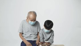 Senior Asian man with surgical face mask watching smartphone screen with his grandson. A 95 years old guy doing a video call due to the covid-19 virus pandemic.