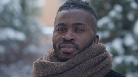 Headshot of confident serious African American man standing on winter day outdoors looking away and turning to camera. Close-up portrait of handsome elegant tourist posing on cold backyard