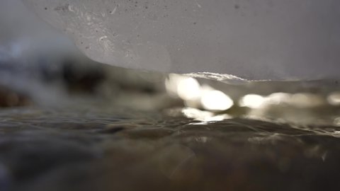 Close up of snow and ice dripping water drop into mountain stream slow motion
