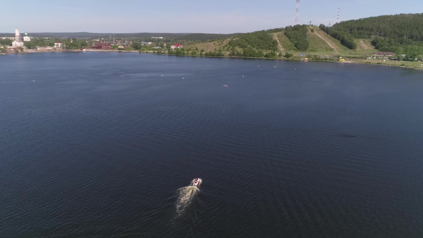 Aerial view of man ride on jetski on the pond in provincial city. People at paddle surfing and paddle boarding (SUP) and in kayaks. Church, Old Factory, forest, mountain and city beach on the Shore. S