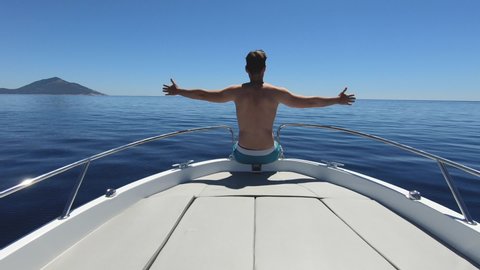 Slow motion - Man spreading out his arms while sitting on the front of the speedboat. Young adult male enjoying fast ride on a motorboat. Feeling alive, energised and free concept