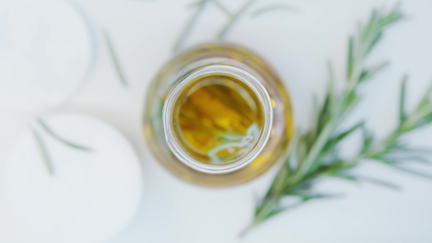 Oil drops from pipette into bottle.  Cosmetics oils based on natural ingredients. Close up glasses bottle with natural oil and green herbs on white table. Top view. Essential oil. Cotton pads. | Shutterstock HD Video #1074755501