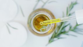 Oil drops from pipette into bottle.  Cosmetics oils based on natural ingredients. Close up glasses bottle with natural oil and green herbs on white table. Top view. Essential oil. Cotton pads. - Powered by Shutterstock - Get 15% off with code: PIKWIZARD15