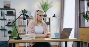 Portrait of good-looking confident experienced light-haired woman in glasses which wears headset during online conference on laptop with coworkers or clients
