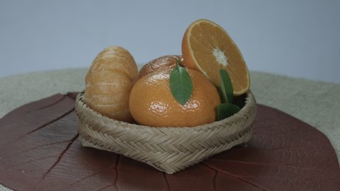 Ripe tangerines in basket made by indigenous people from the Brazilian Amazon Rain forest. A sliced ​​tangerine. Burlap tablecloth on the table. Studio shot, with 360° rotation movement. Take 3.