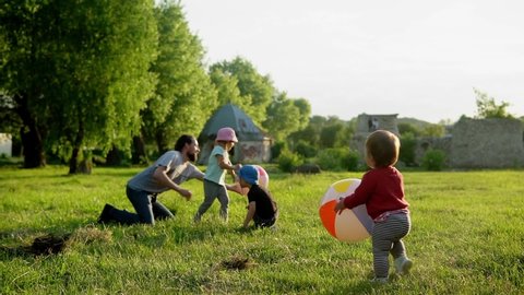 summer, vacation, nature, happy family, childhood, paternity, father Day - Dad with small preschool toddler children kids run have fun playing with big inflatable ball in park at sunset outside