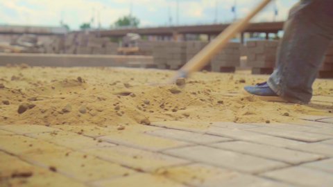 The final stage of laying paving slabs is filling the gaps with dry sand. A construction worker throws sand on concrete tiles with a shovel.