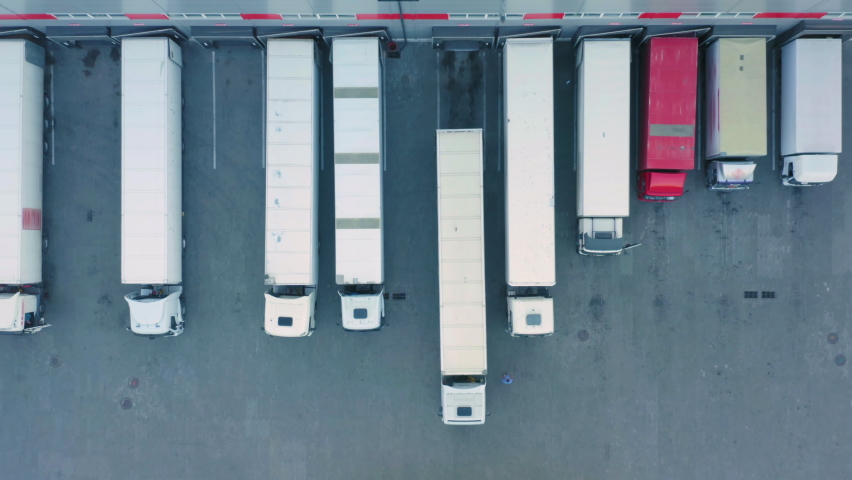 Aerial top down view of semi-trailer trucks standing at a warehouse ramps for loading and unloading goods in a logistics park | Shutterstock HD Video #1074762866