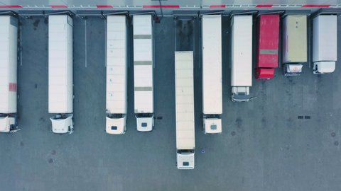 Aerial top down view of semi-trailer trucks standing at a warehouse ramps for loading and unloading goods in a logistics park