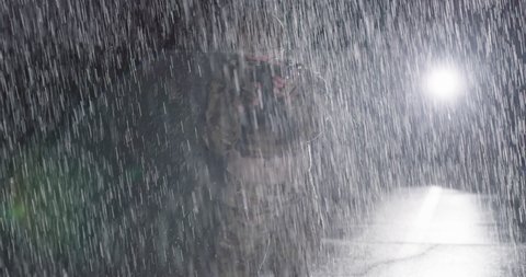 Close-up heavy raindrops on soldier in camouflage on the night, taking military action, aiming weapon sight, and looking straight ahead powerfully and calmly
