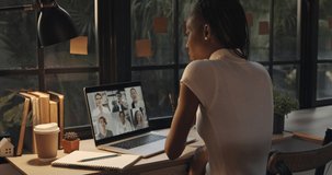 Young African American woman talking with colleagues online via video calling on laptop computer at home during pandemic, dolly shot  