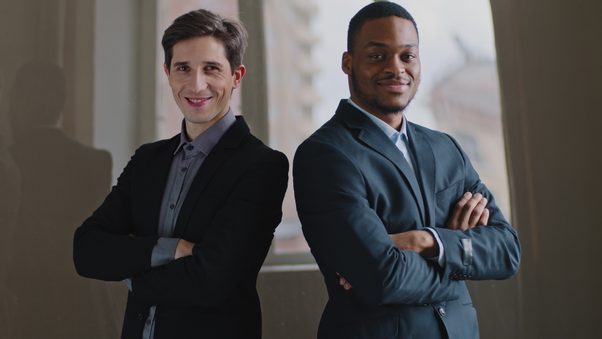 Two multiracial colleagues posing in office with crossed arms, caucasian millennial male showing thumb up symbol of consent approval success, afro american business man pointing index finger at camera Royalty-Free Stock Footage #1074768506