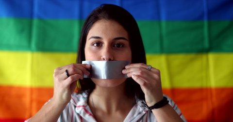 Young woman covering mouth with duct tape. LGBT censorship concept. Gay girl removing tape