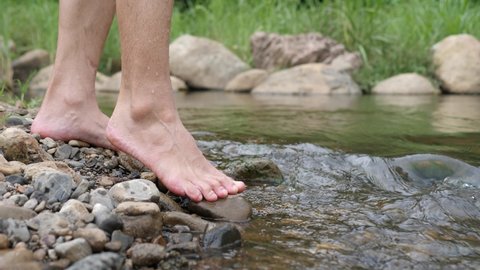Male feet walking in water river flowing through the mountains.