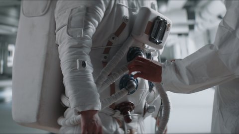 Crew member performing pre-flight inspection on a female astronaut space suit, rocket launch preparation check-up. Shot with 2x anamorphic lens