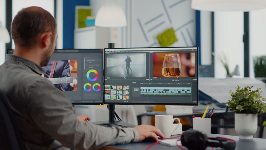 Videographer putting on headset editing video project using post production software working in in digital multimedia company with two monitors. Retoucher processing audio film montage on computer